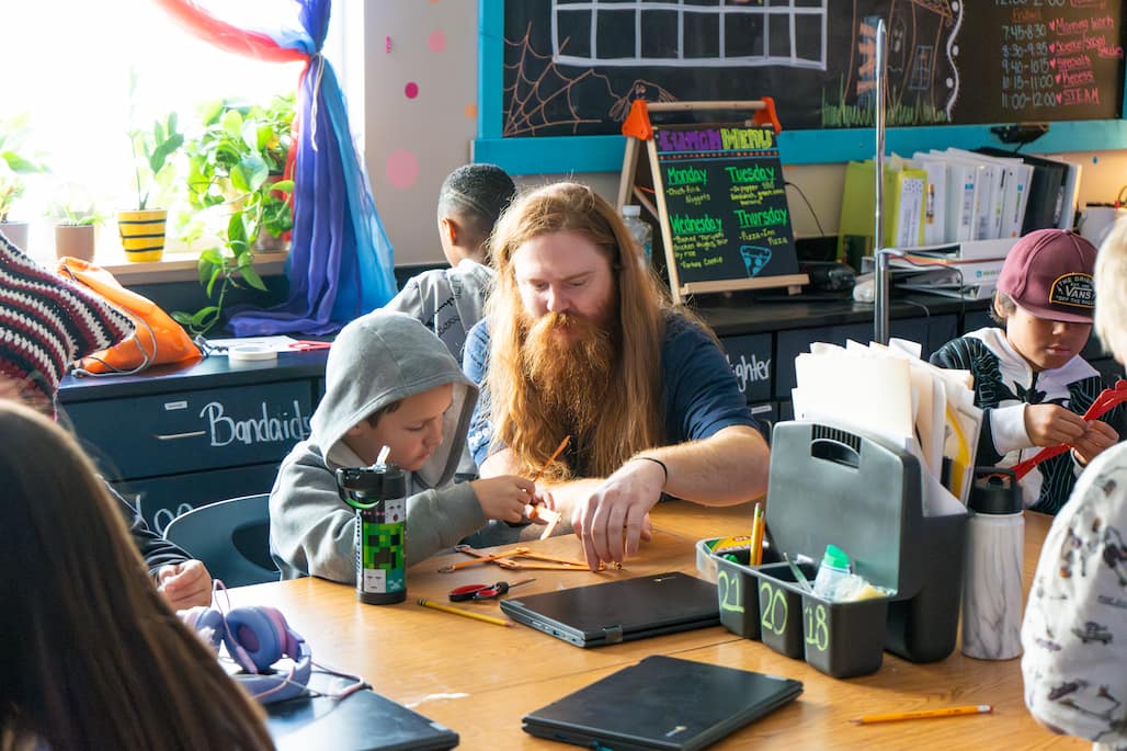 Photo of a person helping a young child make a robot arm out of popsicle sticks.