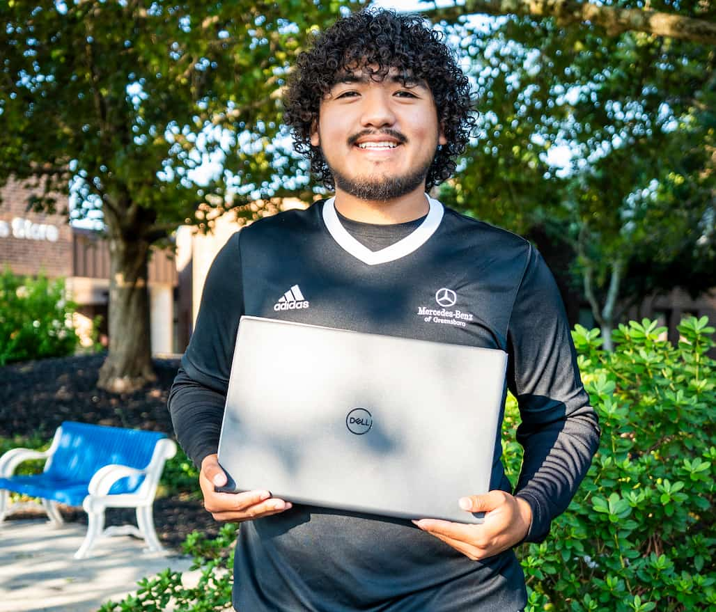 Photo of a person standing in a garden holding a laptop.