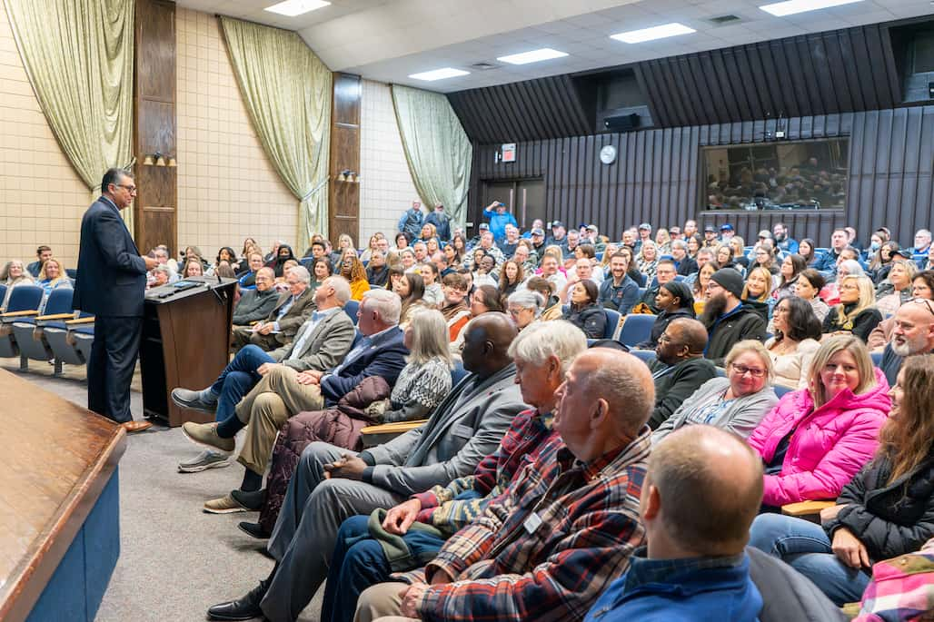 Photo of a person standing at a podium and speaking to an audience in an auditorium.