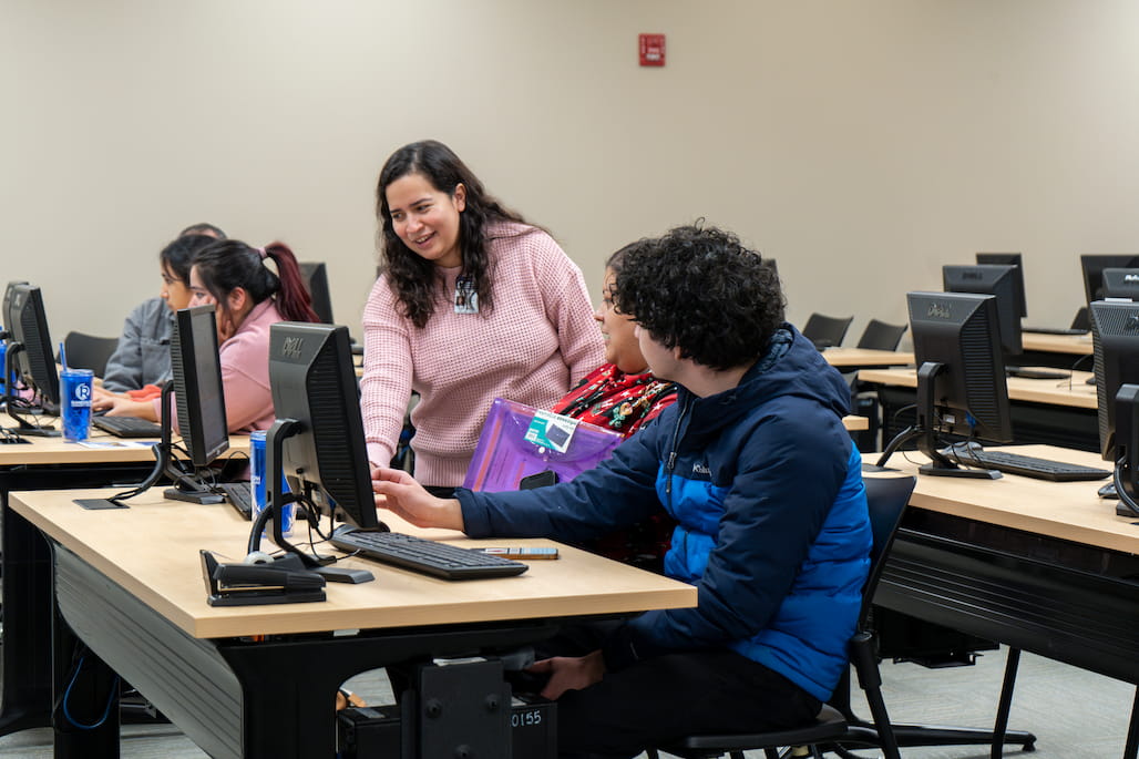 Photo of a person helping another person sitting at a computer.